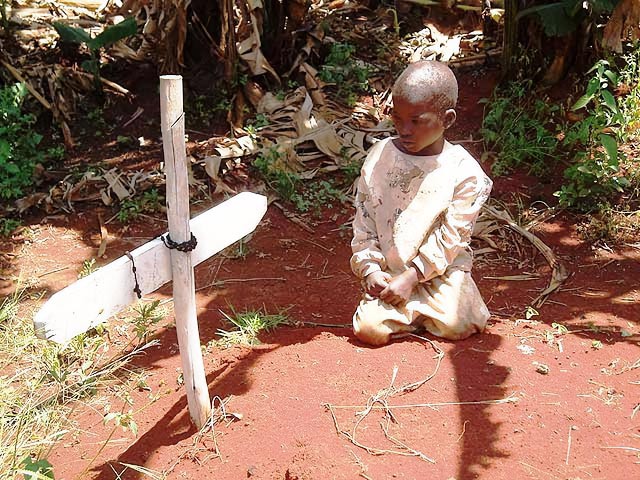 Young African orphan boy kneeling by a grave marked with a cross